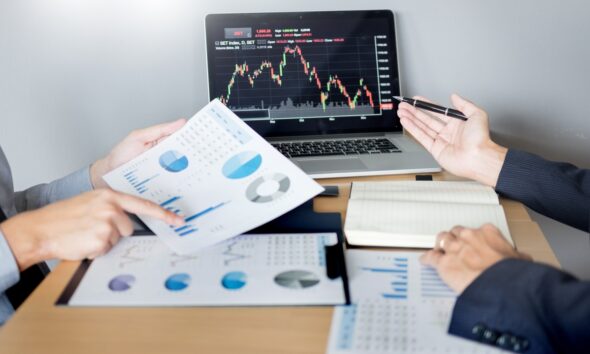 Empresários conversando com gráficos nas mãos e no computador, fazendo estudo de viabilidade