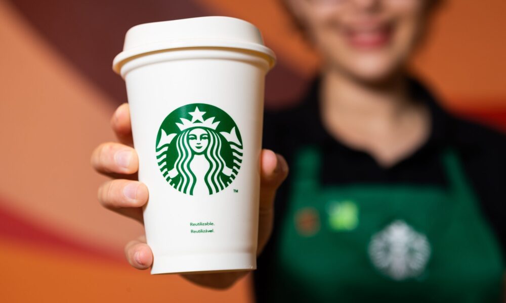 atendente do Starbucks segurando copo da rede; Zamp negocia para assumir operações da marca no Brasil