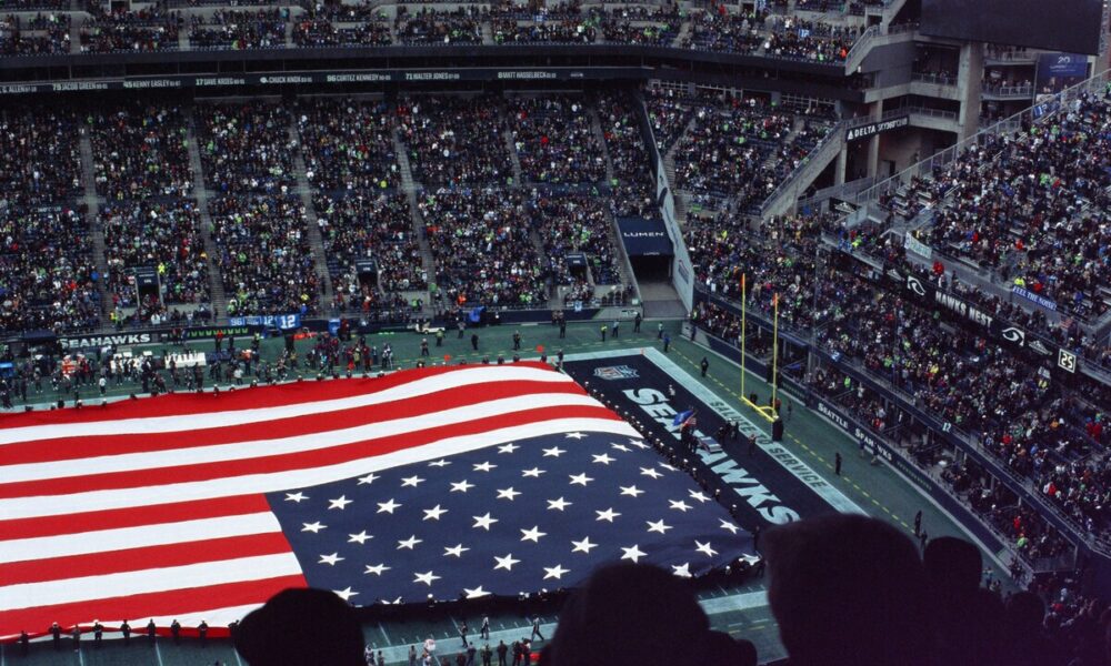 Visto de cima, estádio com plateias lotadas e, no lugar do campo, uma bandeira gigante dos Estados Unidos