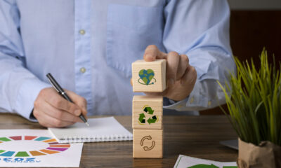 Homem escrevendo com uma mão, e empilhando blocos de madeira com símbolos de sustentabilidade