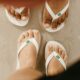 Chinelos havaianas brancos com bandeira brasileira nos pés de duas mulheres. Alpargatas