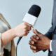 Jornalista segurando microfone para fala de entrevistado. Close nas mãos. Imprensa