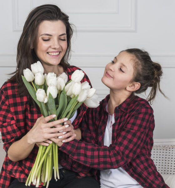 Menina presenteando mãe com flores no dia das mães. As duas usam camisas xadrez vermelhas iguais