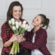 Menina presenteando mãe com flores no dia das mães. As duas usam camisas xadrez vermelhas iguais