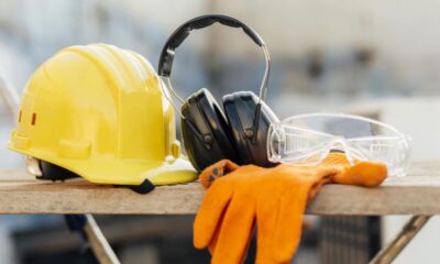 Equipamentos de segurança de trabalho: capacete amarelo, fones de ouvido para ruído, luvas, óculos transparentes.