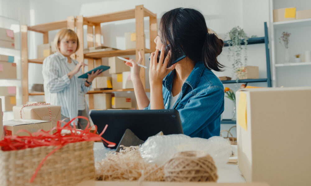 Jovens empresárias da Ásia usando chamadas de celular recebendo pedidos de compra e verificando o produto em estoque trabalham no escritório doméstico. Proprietário de pequena empresa, entrega no mercado on-line, conceito freelance de estilo de vida.