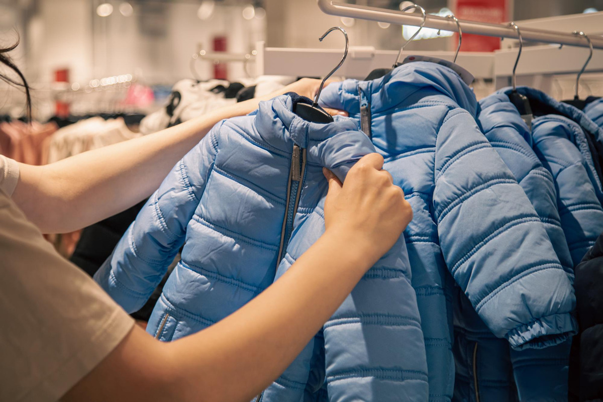 mulher colocando roupa de frio em arara em loja