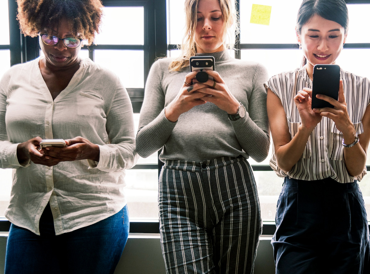 três mulheres em pé mexendo no celular